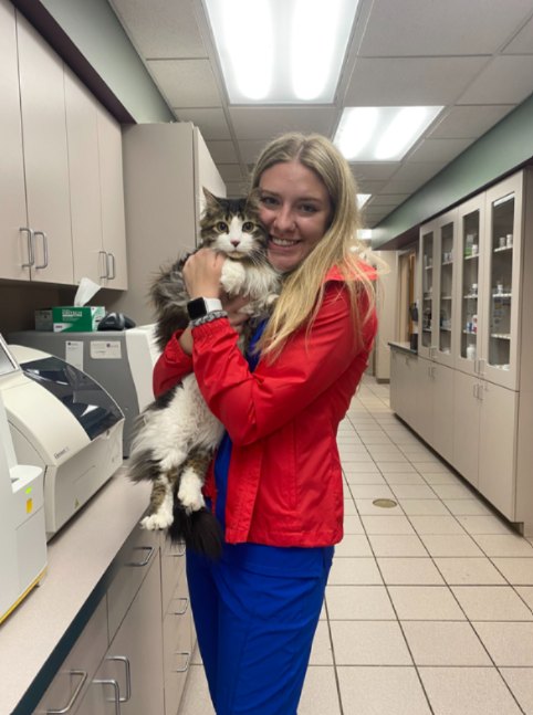 Vet tech in a red jacket hugging a fluffy tabby cat