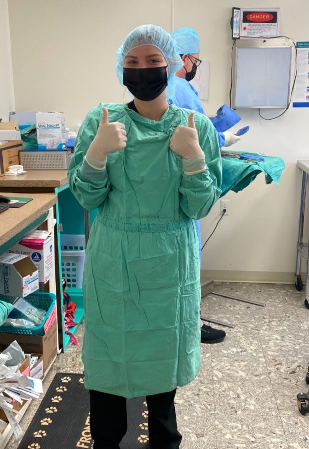 Vet tech in a surgical gown and cap giving two thumbs up